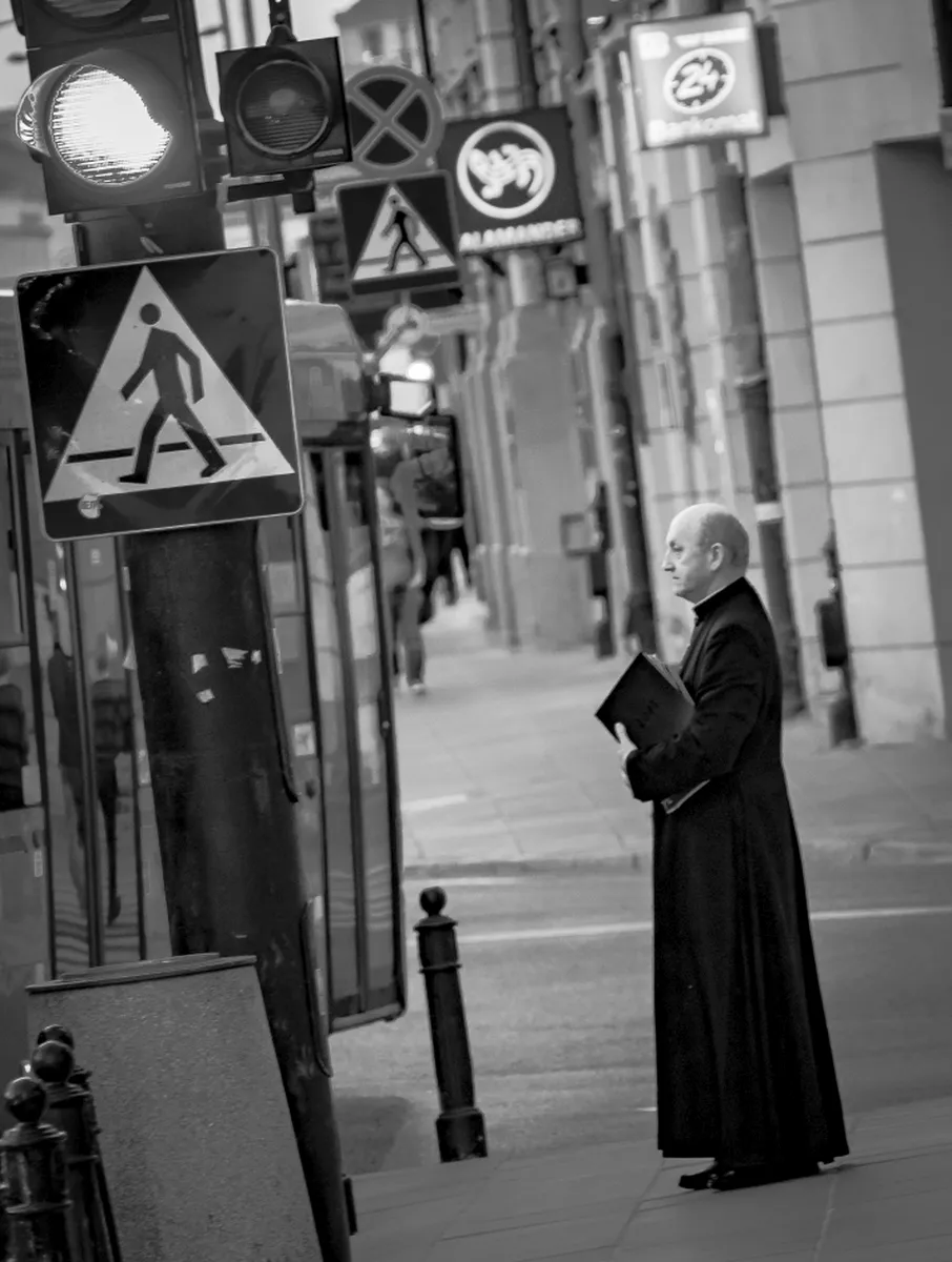 Priest in a long black cassock standing beneath clustered street signs